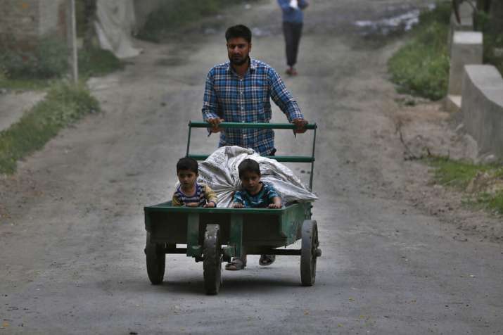 A Kashmiri farmer pushes a handcart with children on it on